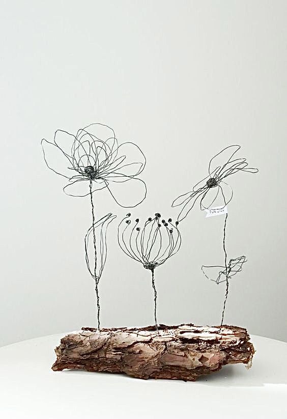 three metal flowers sitting on top of a piece of driftwood in front of a white wall