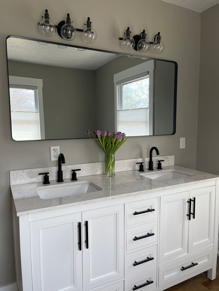 a bathroom vanity with two sinks and a large mirror above it, in front of a window