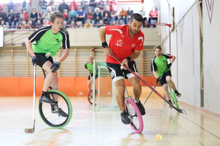 two men riding unicycles in an indoor arena