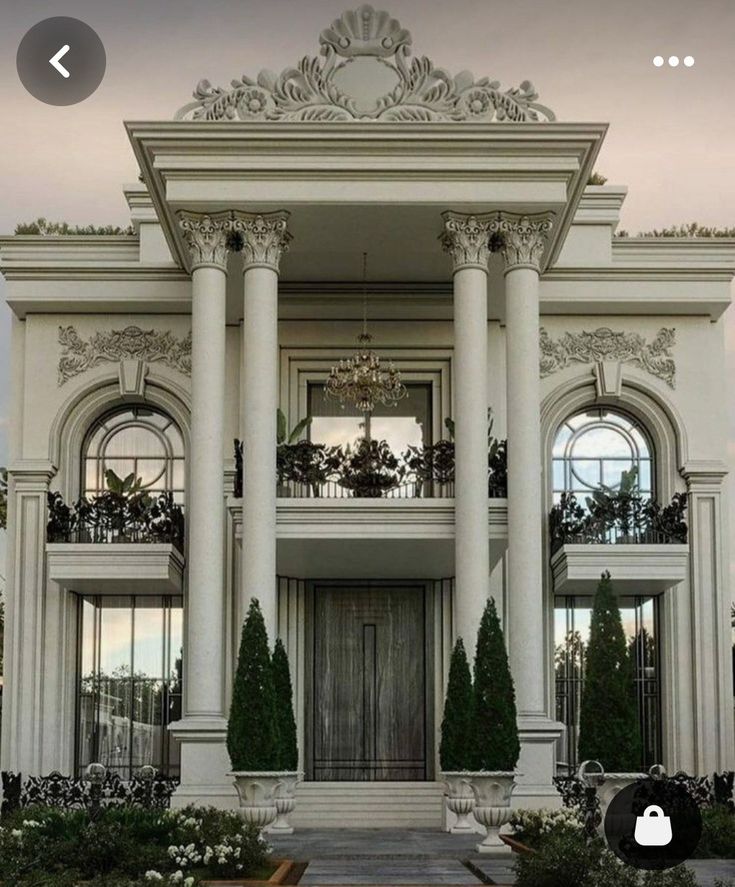 a large white house with columns and windows on the front door, surrounded by greenery