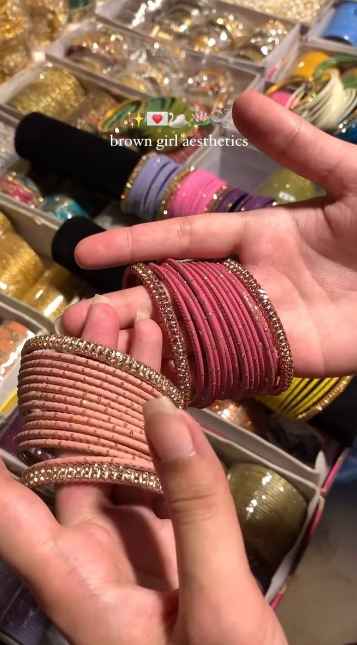 two hands are holding bracelets in front of some other jewelry and accessories on display