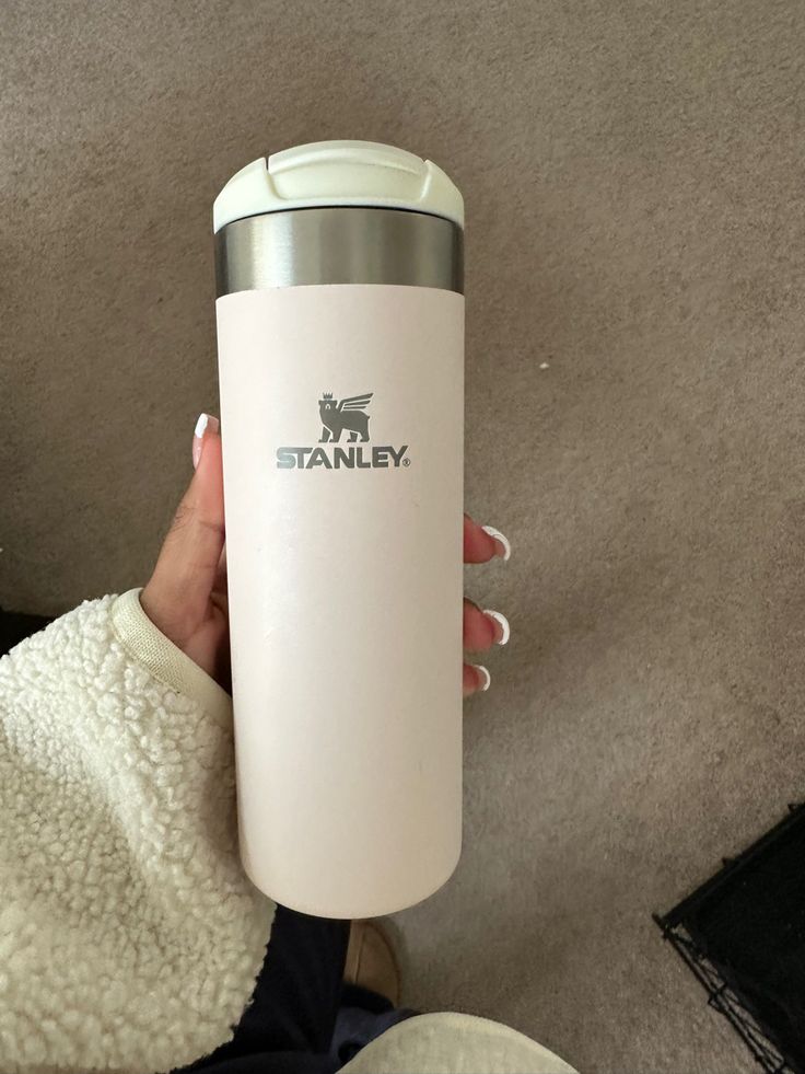 a woman holding a white travel mug in her hand with the word stanley on it