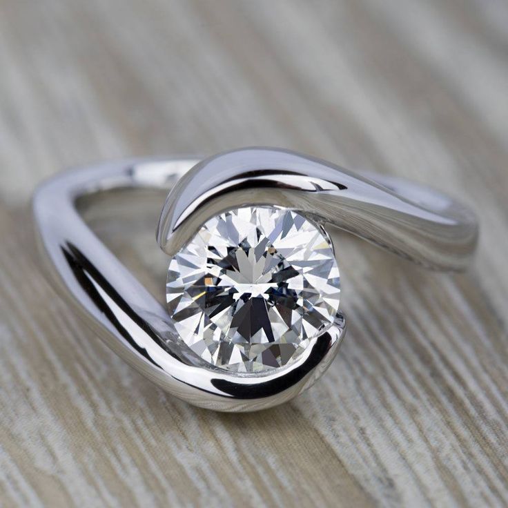 a white gold ring with a round diamond in the center, on a wooden surface