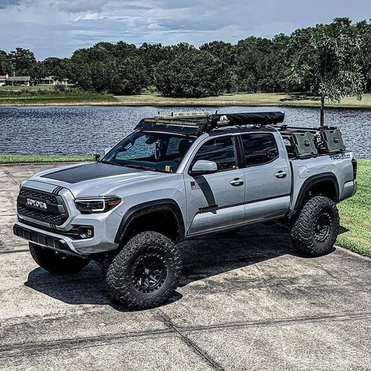 a silver truck parked on top of a cement road next to a body of water