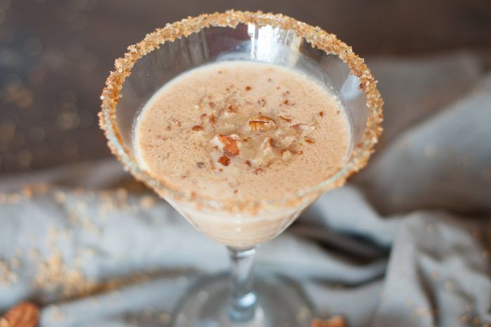 a glass filled with some kind of drink on top of a table next to nuts