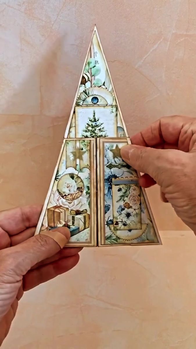 two hands holding an origami christmas tree with ornaments on the top and bottom