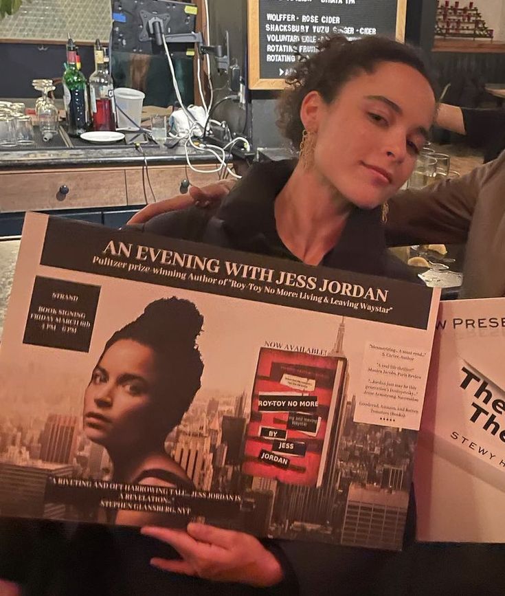 a woman sitting at a table holding up a magazine