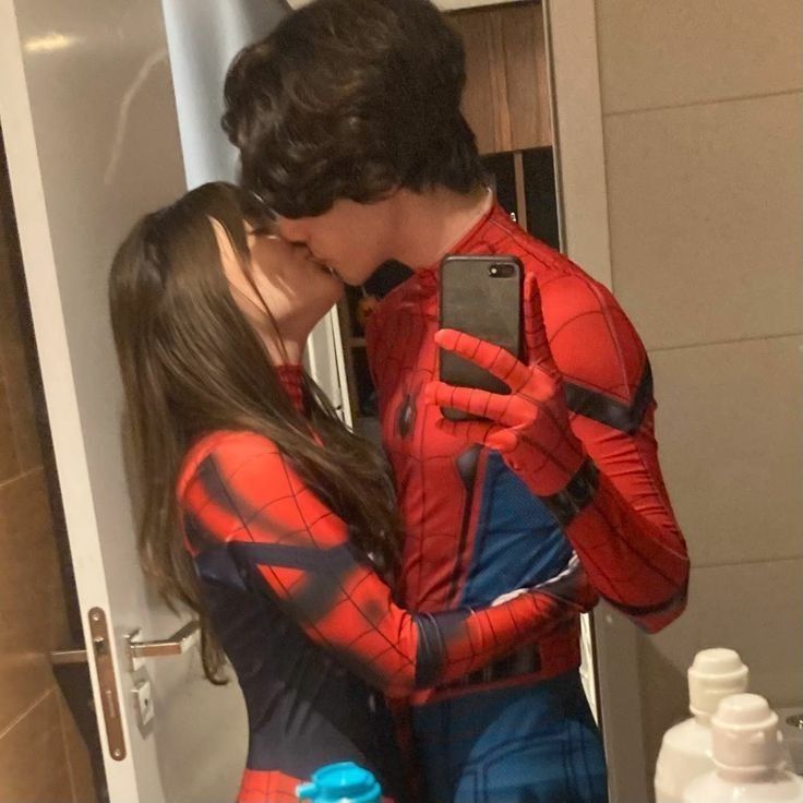 a man and woman dressed as spiderman kissing in front of a bathroom mirror while holding a cell phone