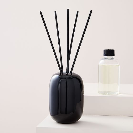 a black vase with sticks sticking out of it next to a bottle of water on a white surface