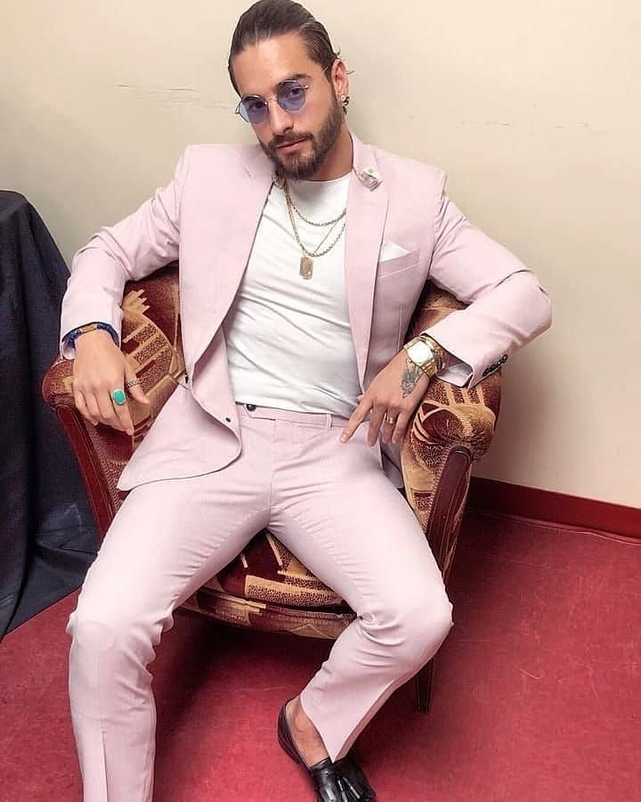 a man sitting in a chair wearing a pink suit and black shoes with his hands on his hips