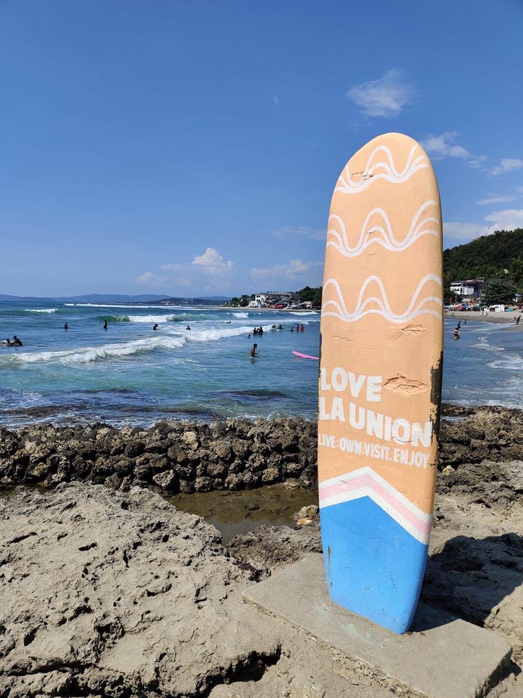 a surfboard sitting on top of a sandy beach next to the ocean with people swimming in the water