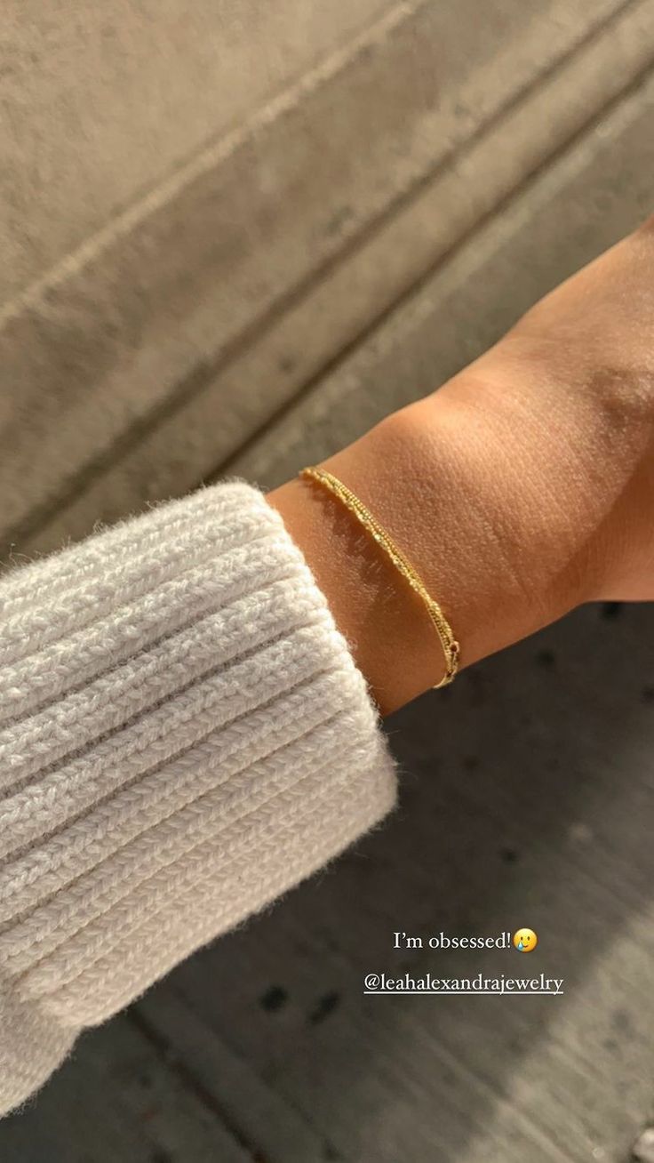 a woman's arm with a gold bracelet on it and a white cardigan sweater