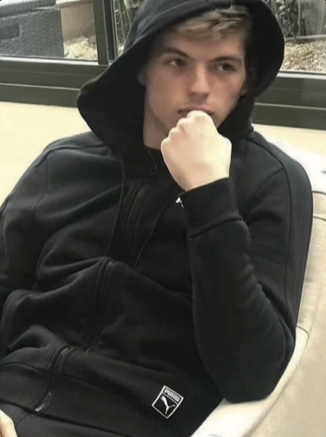 a young man sitting in a chair with his hand on his chin and wearing a black hoodie