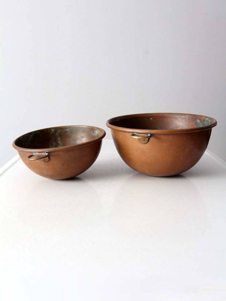 two metal bowls sitting on top of a white counter