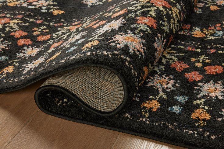 a black rug with flowers on it laying on top of a wooden floor next to a wall