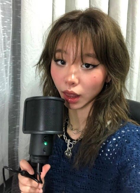 a woman holding a microphone up to her face and making a funny face while sitting in front of a window