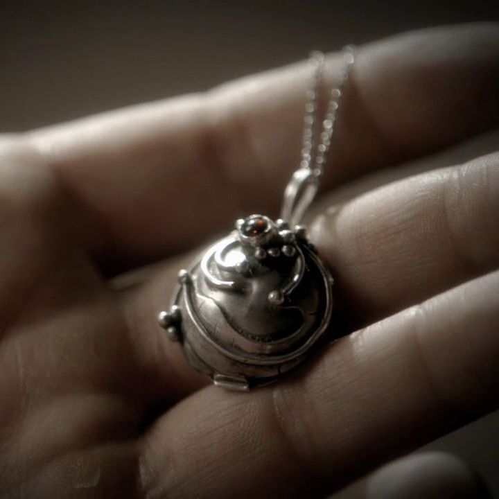 a person holding a tiny silver object in their hand with a chain attached to it