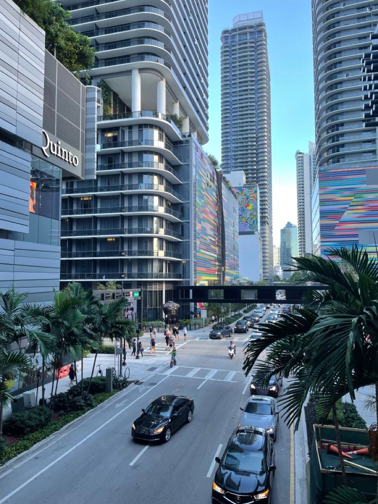 cars are driving down the street in front of tall buildings and palm trees on either side