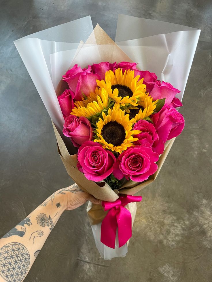 a bouquet of sunflowers and pink roses wrapped in paper with a tattoo on the arm