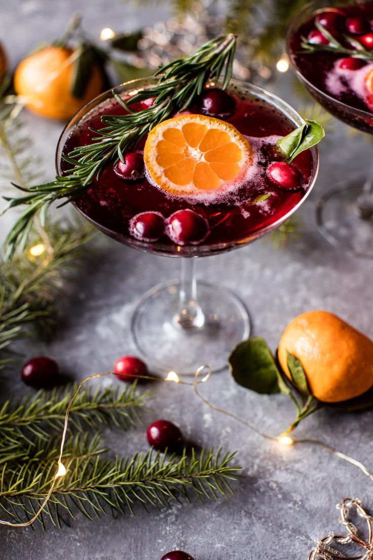 two glasses filled with wine and garnished with orange slices, rosemary and cranberries