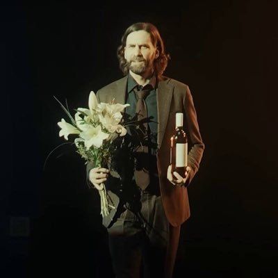 a man in a suit and tie holding a bouquet of flowers next to a bottle of wine