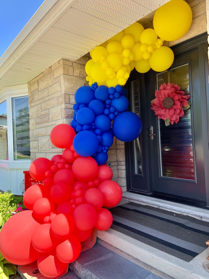 a bunch of balloons that are on the side of a house with flowers in front of it