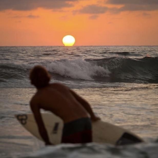 a man sitting on top of a surfboard next to the ocean at sunset or dawn