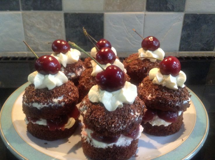 several cupcakes with cherries and whipped cream on top sit on a plate