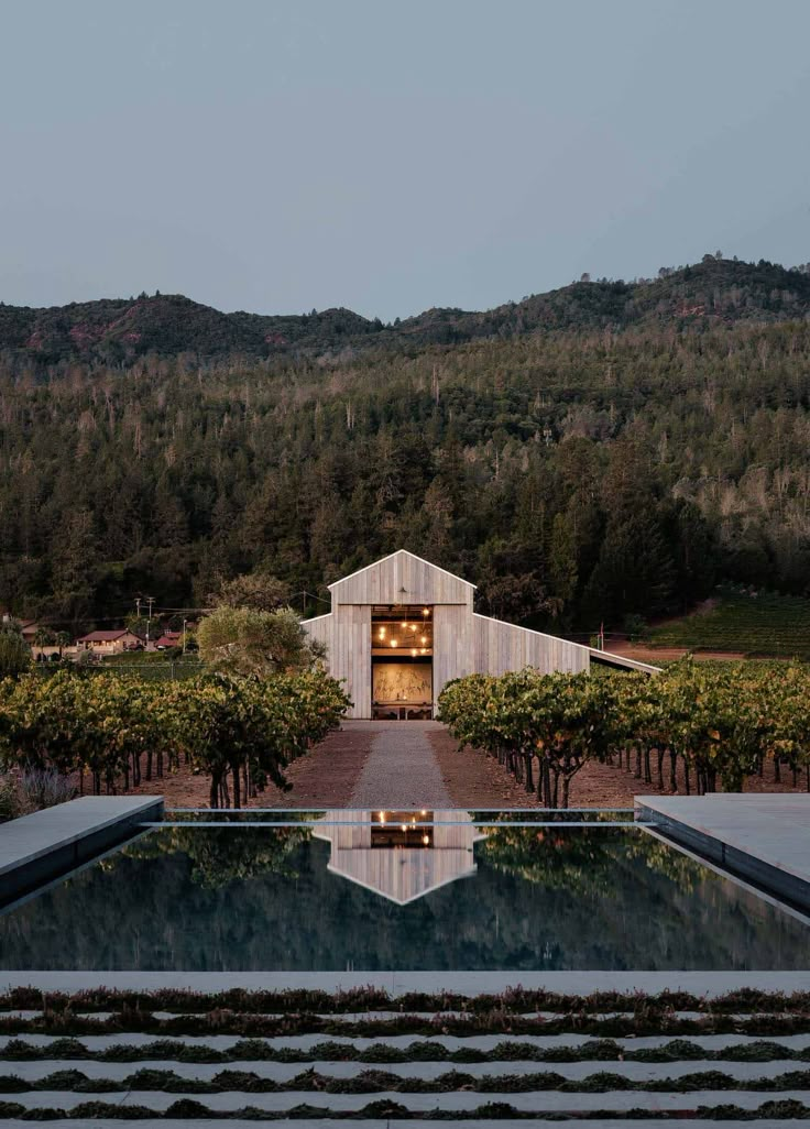 an outdoor pool surrounded by trees and bushes with a barn in the background at dusk