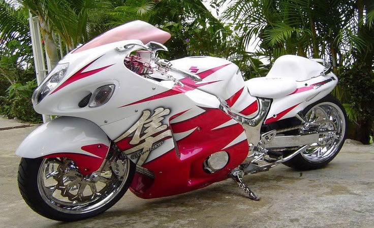 a red and white motorcycle parked on top of a cement ground next to trees in the background