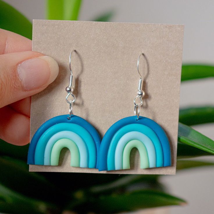 a pair of blue and green earrings sitting on top of a wooden box next to a plant