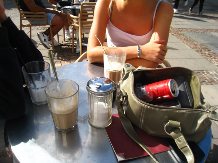 a woman sitting at an outdoor table with her purse and two drinks in front of her