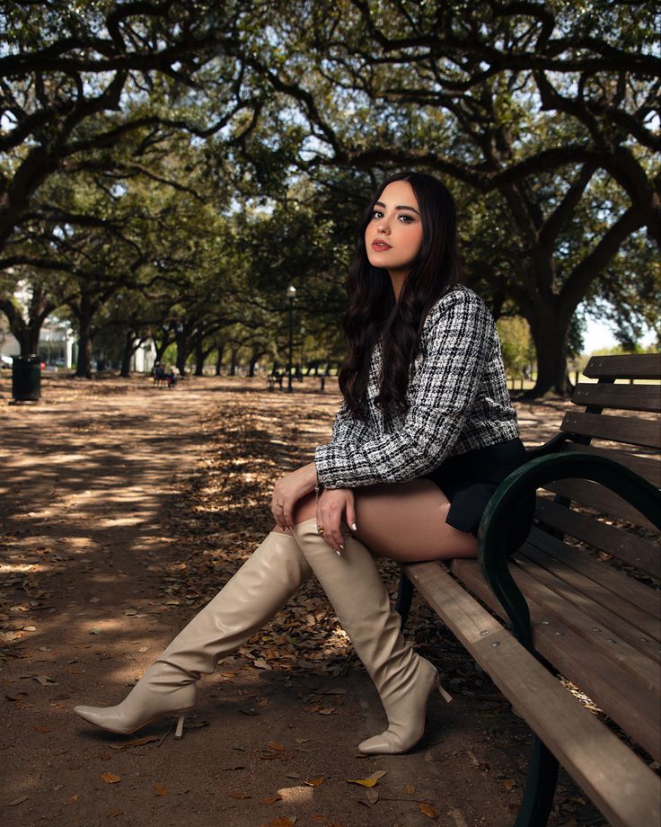 a woman sitting on top of a wooden bench in front of trees and dirt ground