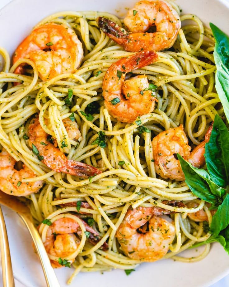 pasta with shrimp and parsley in a white bowl next to gold utensils