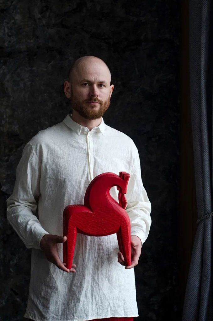 a man holding a red sculpture in front of a black background with the shape of a heart