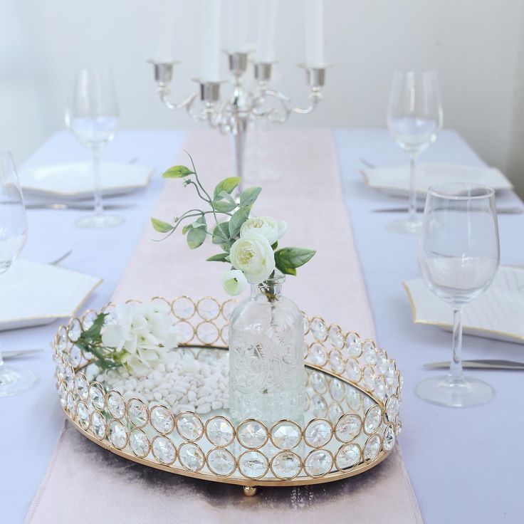 a table topped with a tray filled with white flowers and greenery next to wine glasses