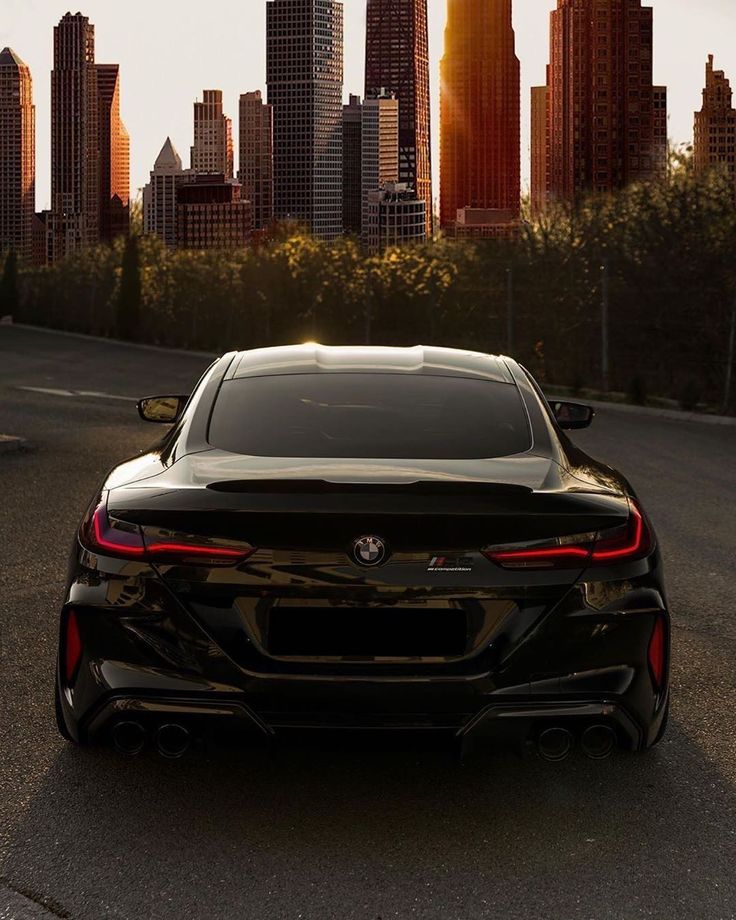 the rear end of a black car in front of a cityscape with skyscrapers