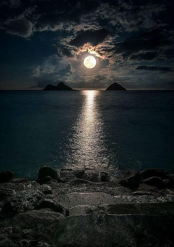 the moon is shining brightly in the night sky over water with rocks and mountains on either side