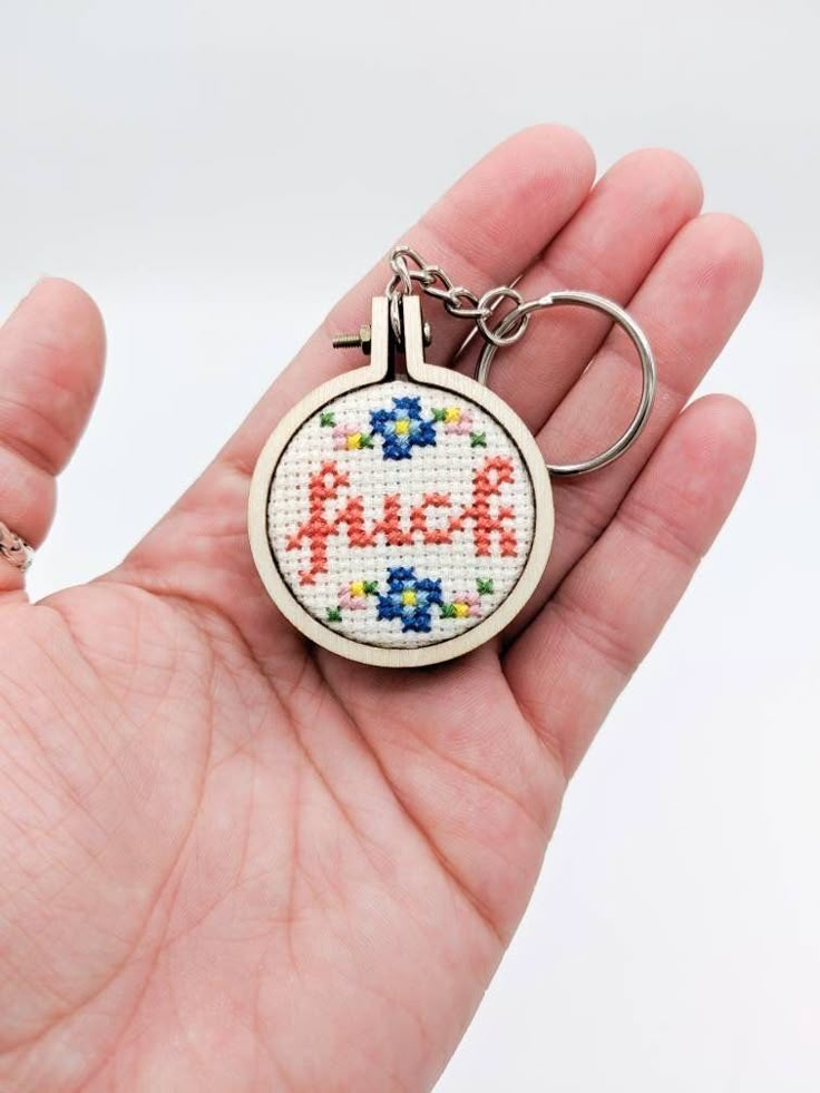 a hand holding a cross stitch keychain with the word alex on it's front