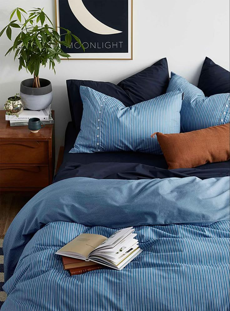 a bed with blue sheets and pillows on top of it next to a potted plant