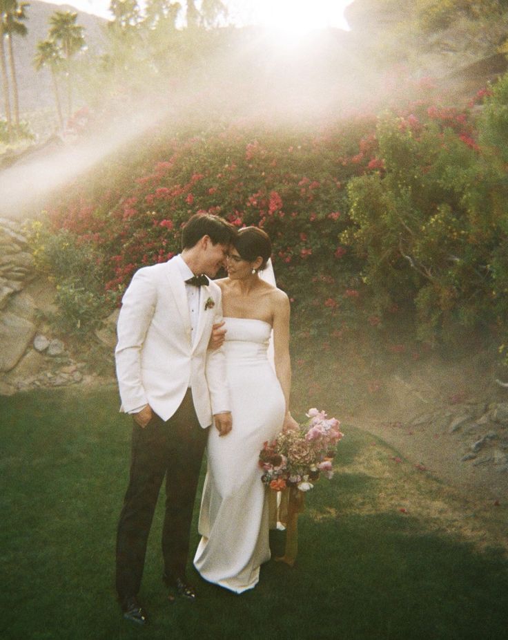 a man and woman in formal wear standing next to each other on grass with flowers