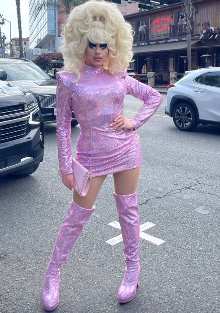 a woman in a purple dress and thigh high boots standing on the street with her hands on her hips