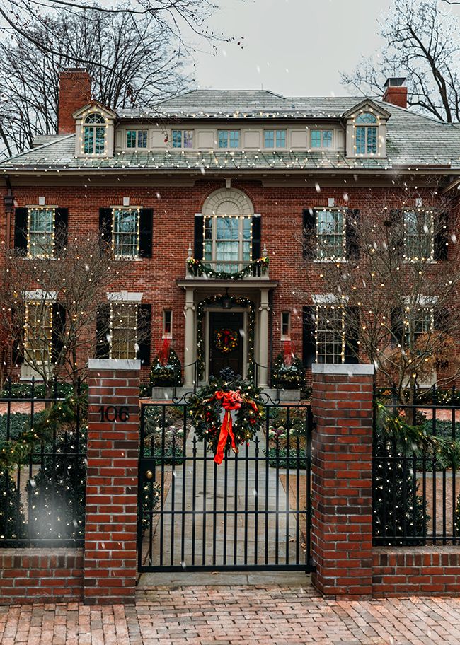 a red brick house with christmas wreaths on the front gate and trees behind it