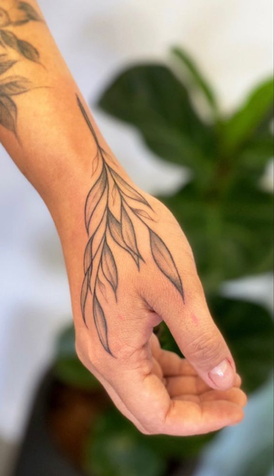 a person's hand with a tattoo on it and a plant in the background