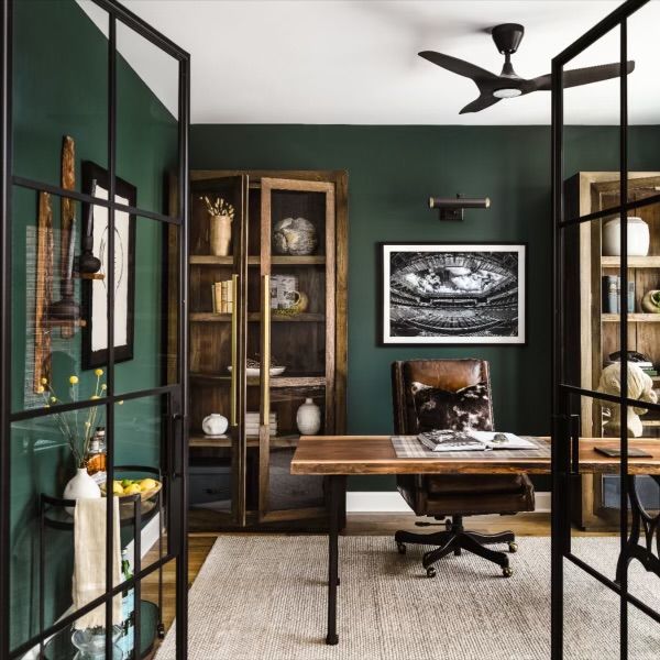 an office with green walls and wooden desk in the center, surrounded by glass partitions