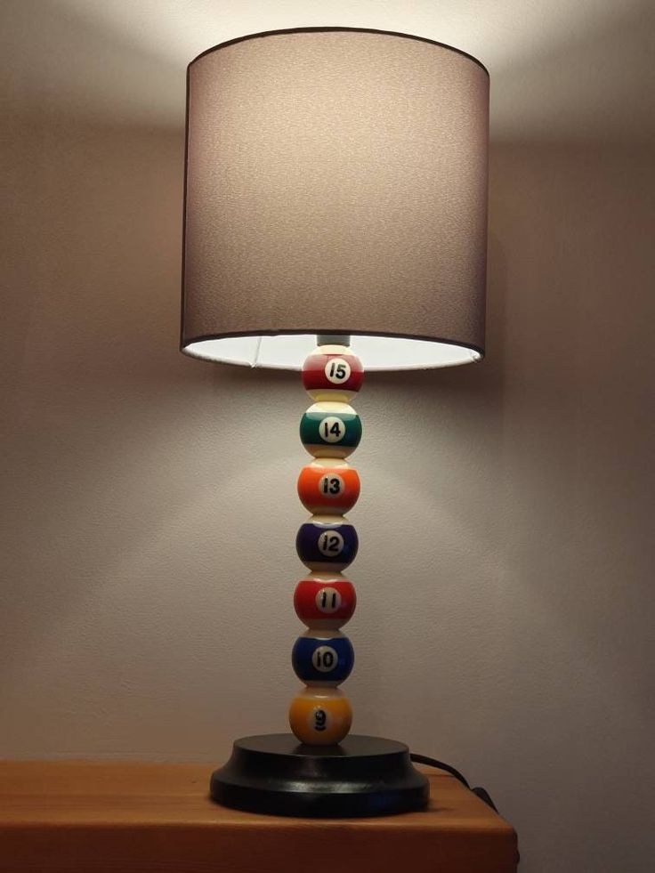 a lamp that is sitting on top of a wooden table next to a dresser with pool balls all around it