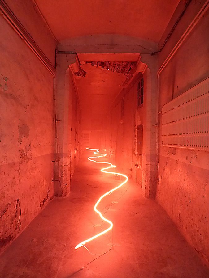 a long narrow hallway with red light coming from the ceiling and pipes running down it