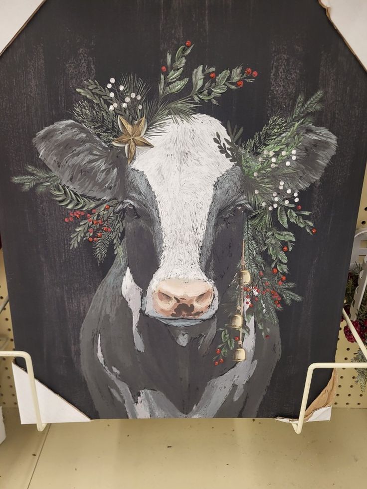 a painting of a cow with christmas decorations on it's head and nose is displayed in a store