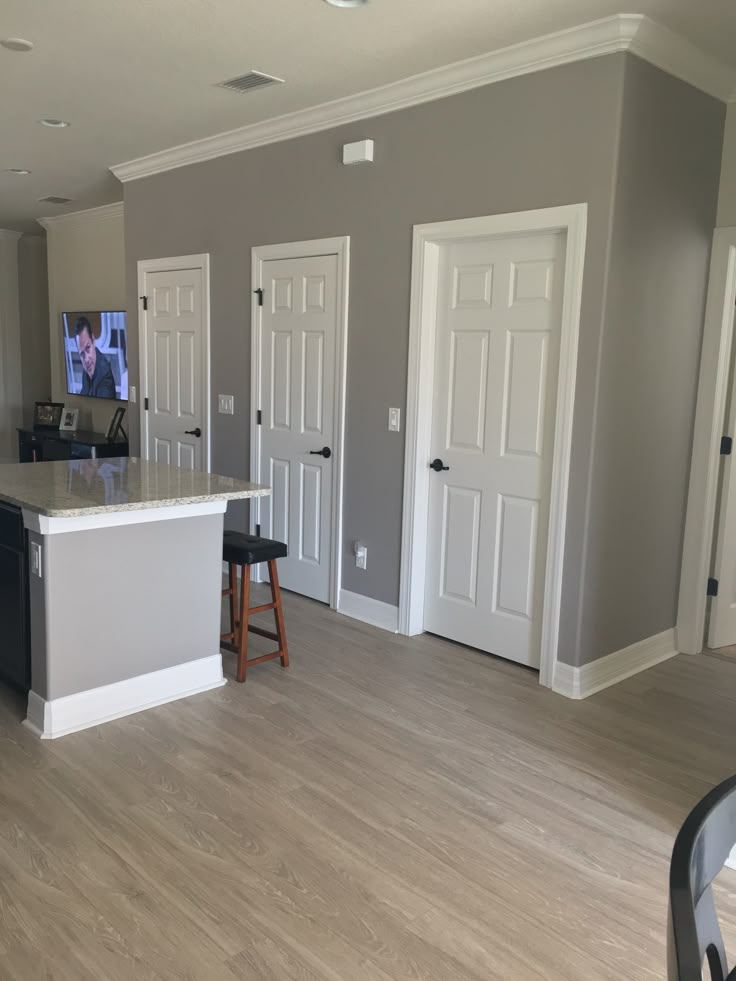 an empty kitchen and living room in a house with gray walls, hardwood floors and white trim