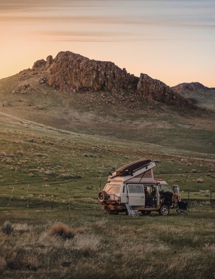 an rv parked in the middle of a grassy field with mountains in the back ground